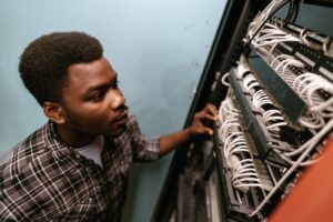 A young adult man in a plaid shirt is shown inspecting a server rack.