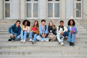 A group of six young adults sits on the wide steps of a building.