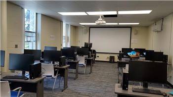 Full room shot of room 219 in the library. An instruction room with computer stations with an area for instruction.