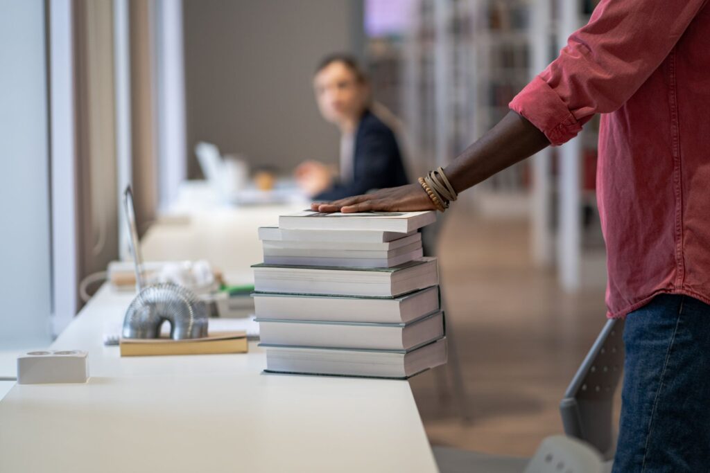 A stack of books sits on a white desk in a modern library setting.