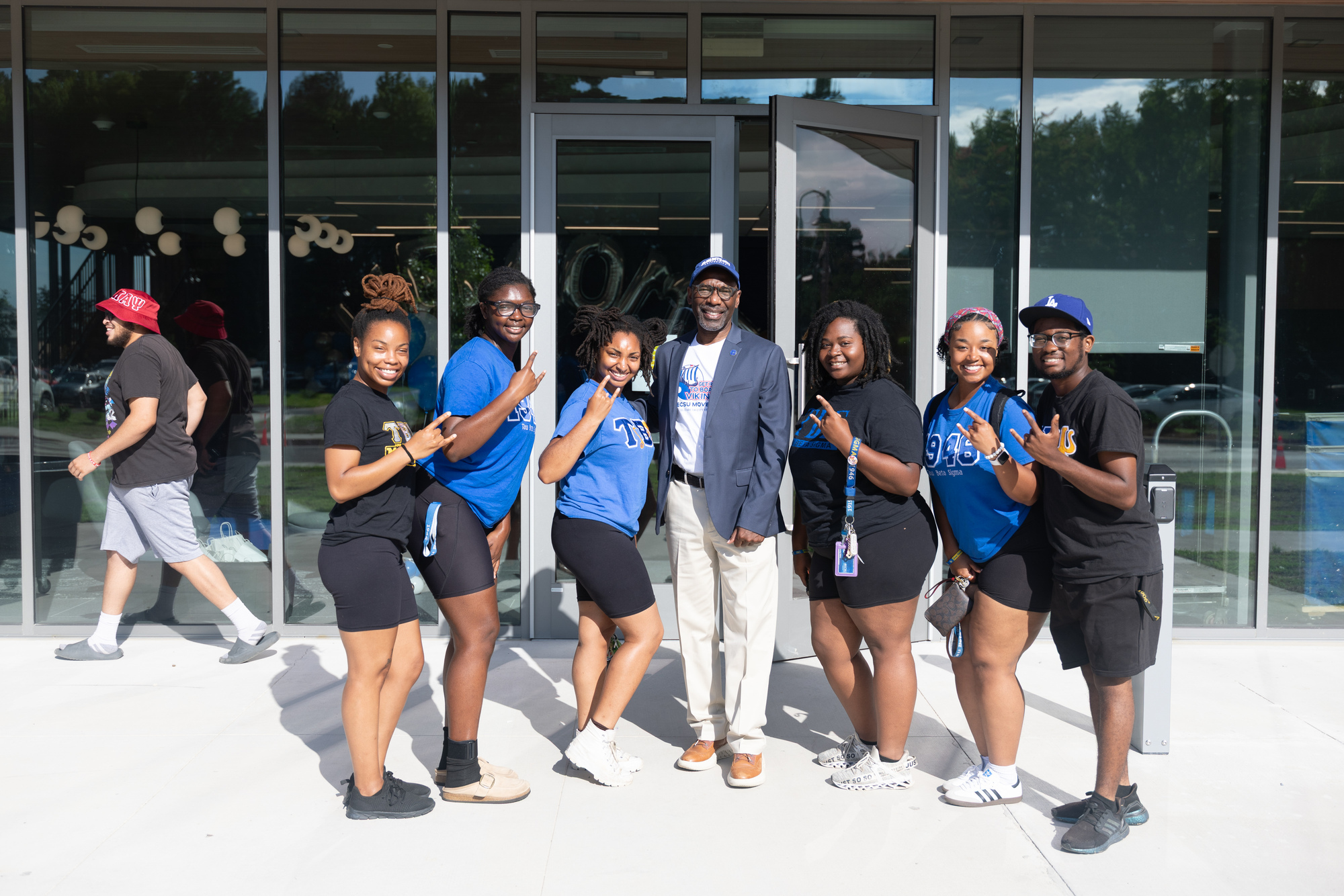 Chancellor Hargrove in the middle of six ECSU students. All are smiling and using Viking Horns hand sign.