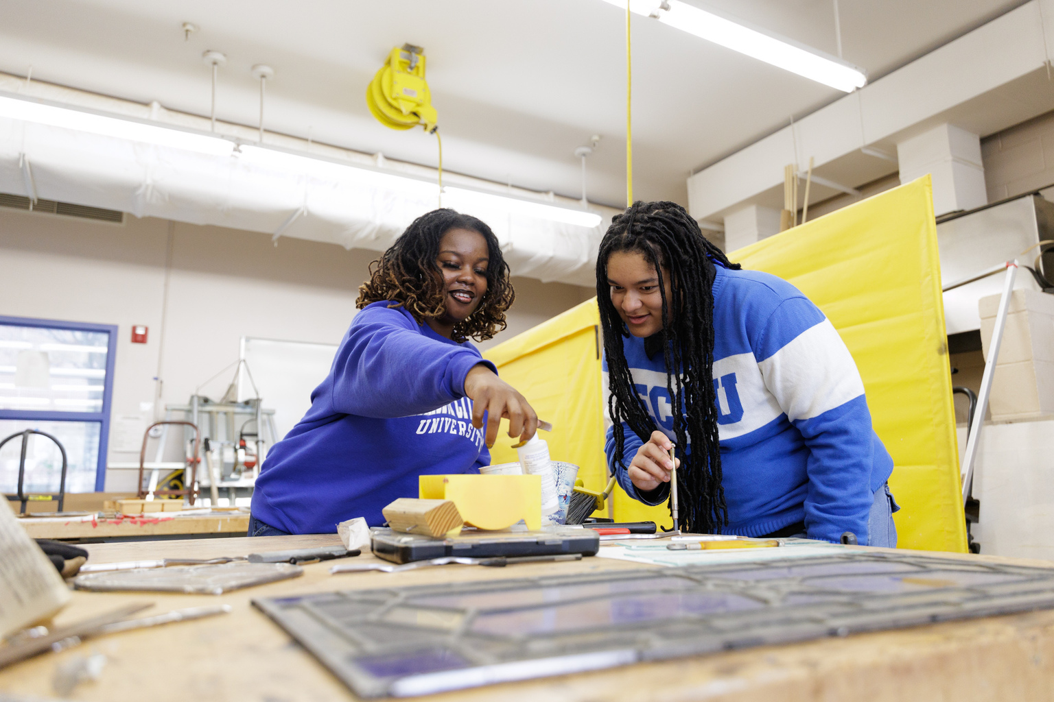Two ECSU students work together at a lab table using tools and materials, examining a small project in a hands-on classroom or workshop setting.
